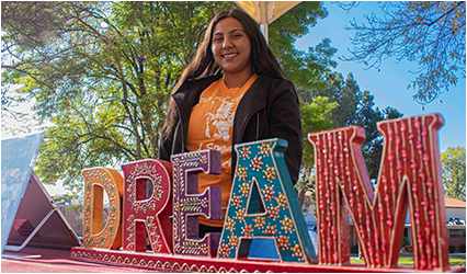 Woman smiling at the camera in front of a decorative sign saying "DREAM"
